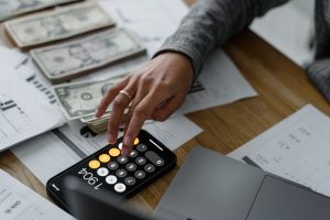 hand of a person using a calculator near cash money on wooden table