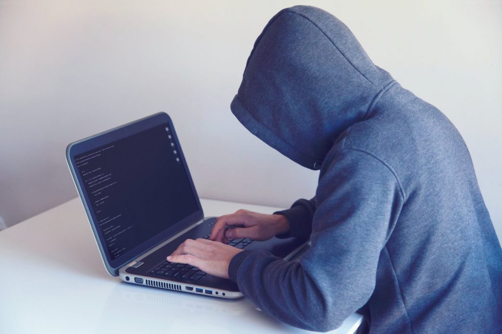 anonymous hacker with on laptop in white room